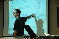 Lecturer in front of a screen with a program projection.